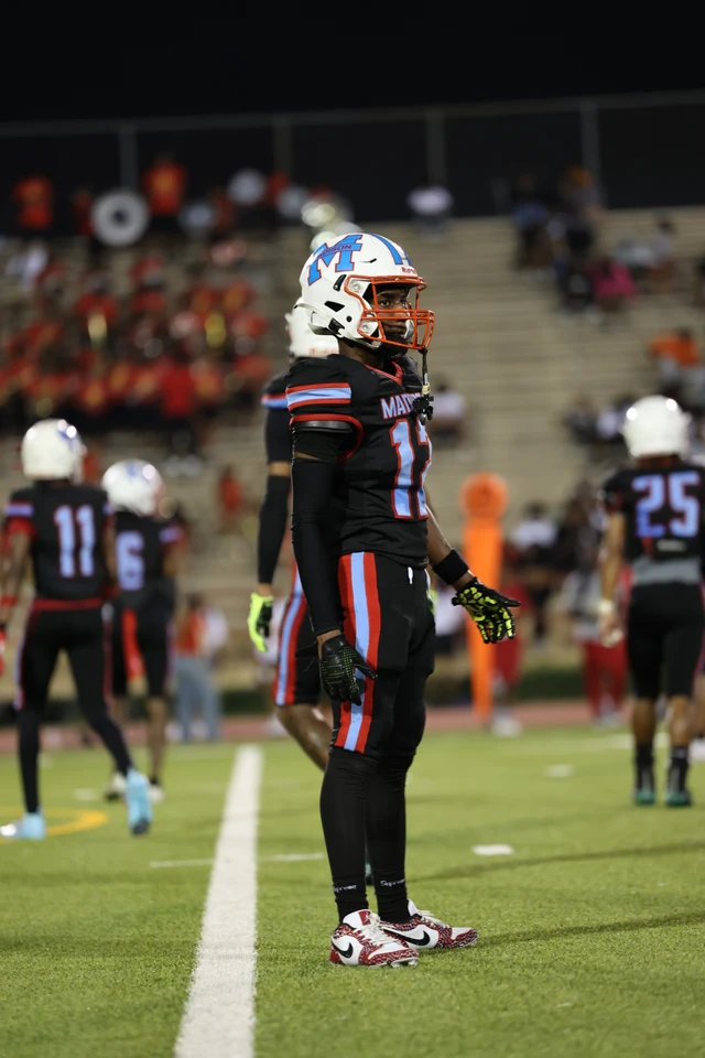 A Madison player in a number 12 jersey watching the field from the sideline at night.
